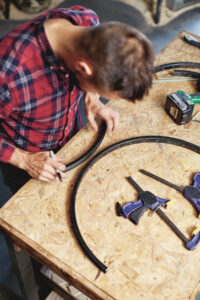 man placing two pieces of cut bicycle rim against each other on a wooden work&hellip;